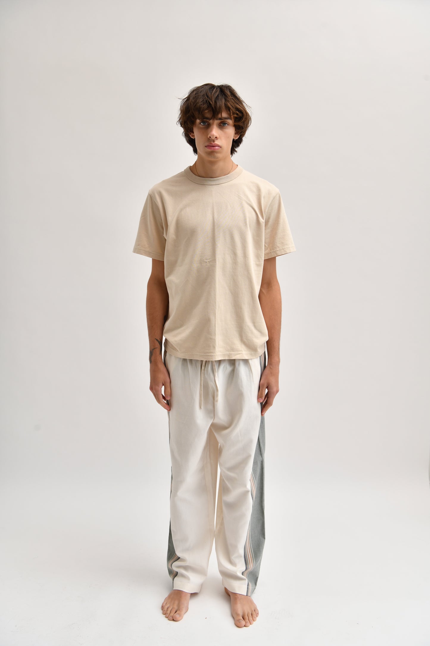 Front image of cream and khaki cotton trousers featuring a wide-leg, relaxed fit with a linen-style drape.