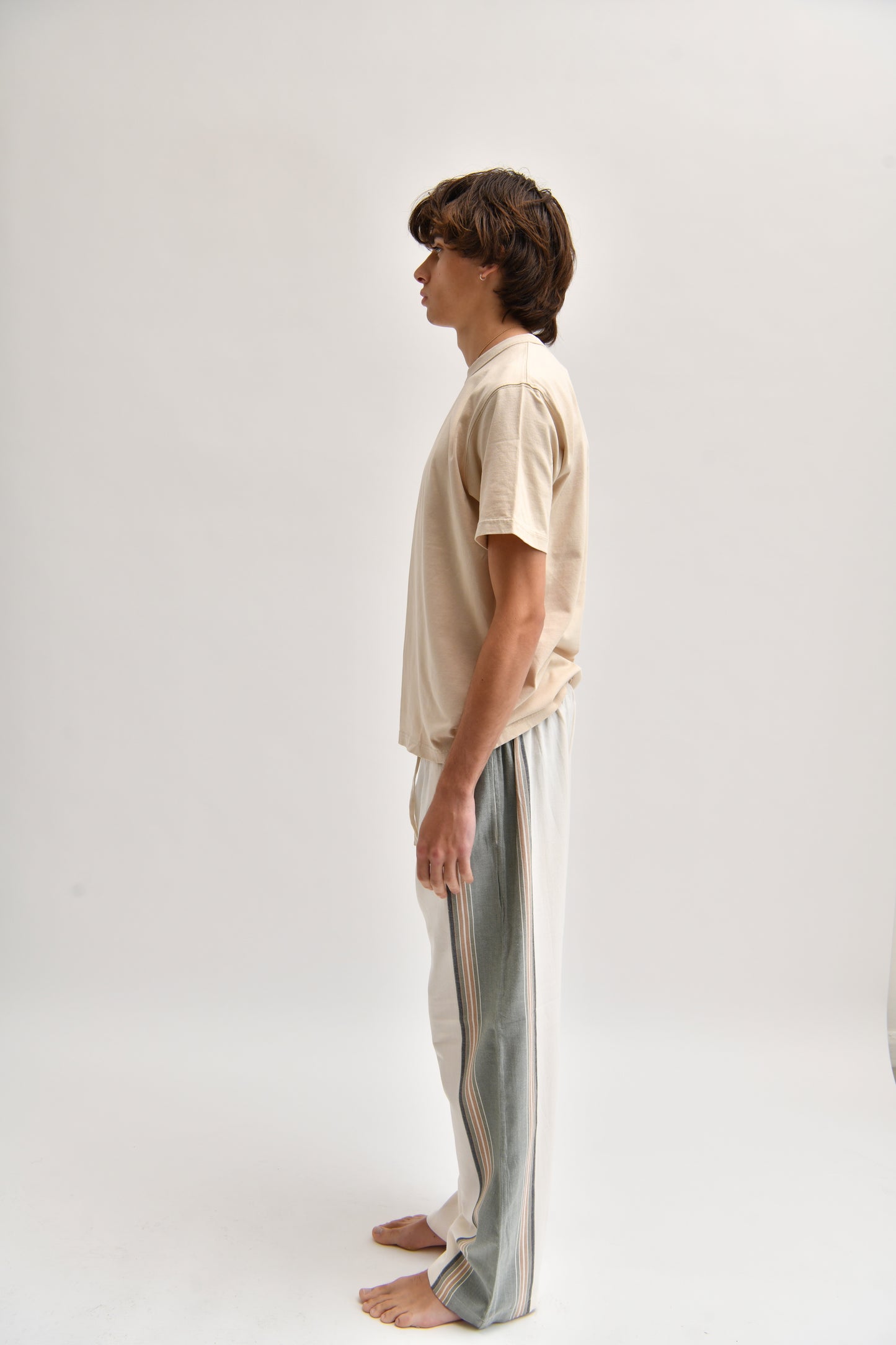Side image of cream and khaki cotton trousers featuring a wide-leg, relaxed fit with a linen-style drape.