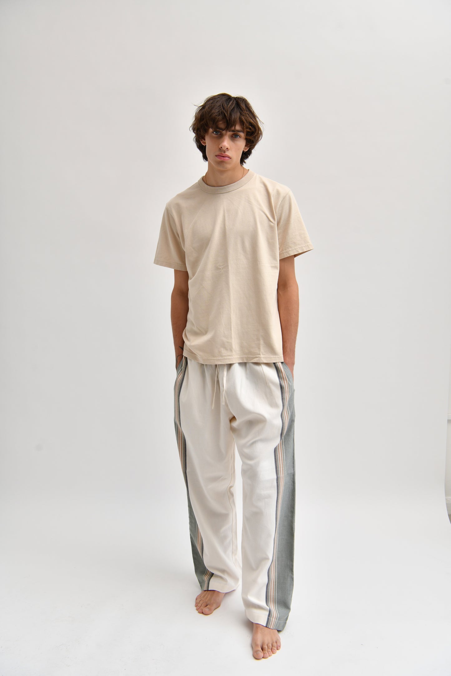 Front image of cream and khaki cotton trousers featuring a wide-leg, relaxed fit with a linen-style drape.